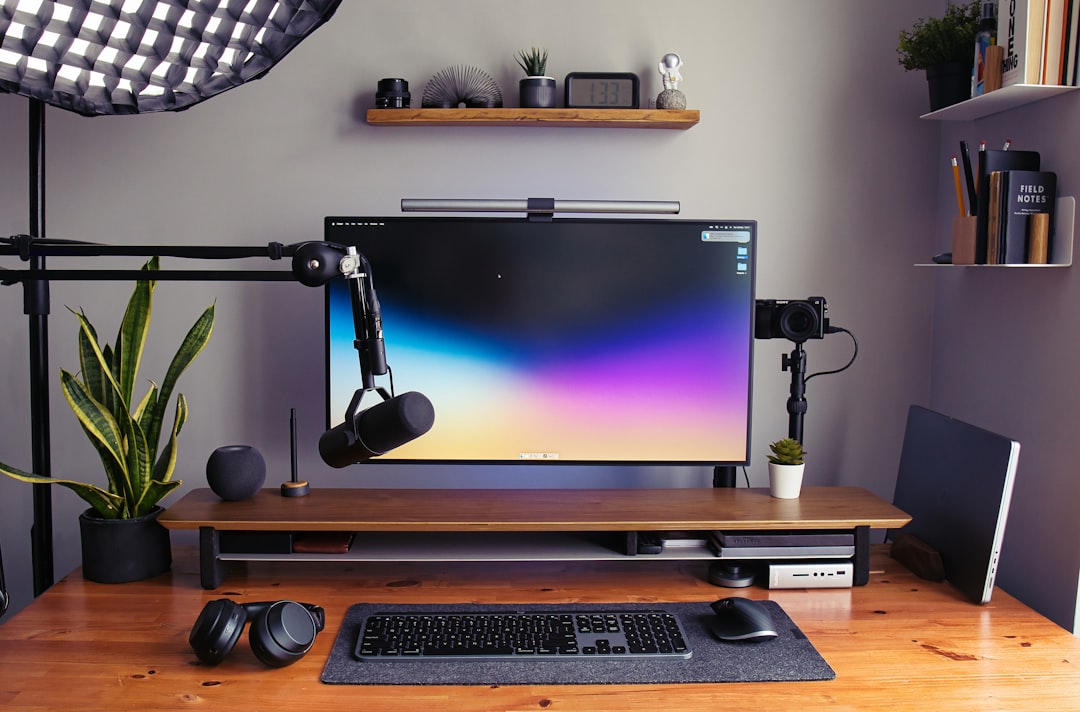 Dual monitor arm clamp mounted to the back of a wooden desk elevating two monitors