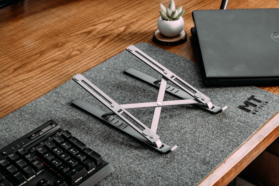 A compact foldable laptop stand supporting a thin laptop on a wooden desk setup